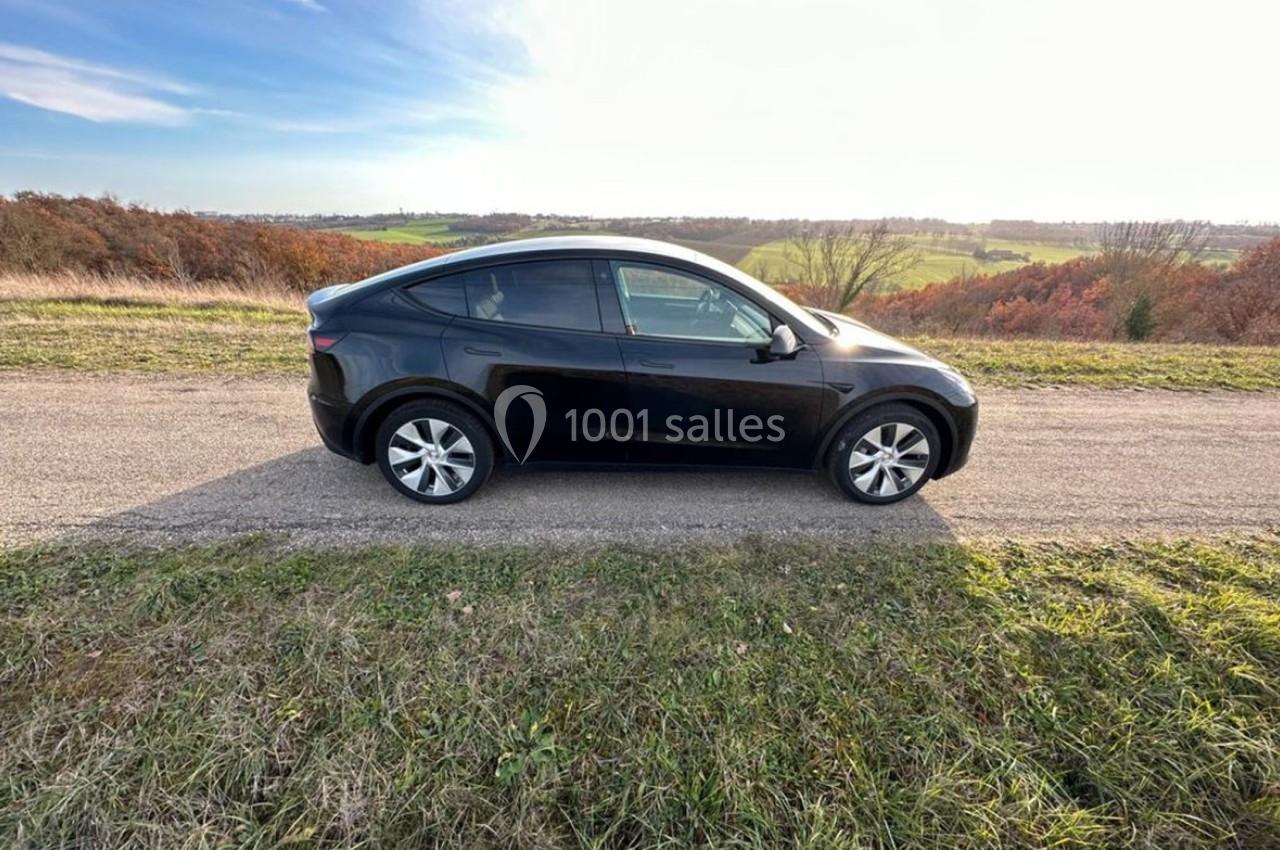 Voiture noire stationnée sur une route de campagne, avec un paysage vallonné en arrière-plan.