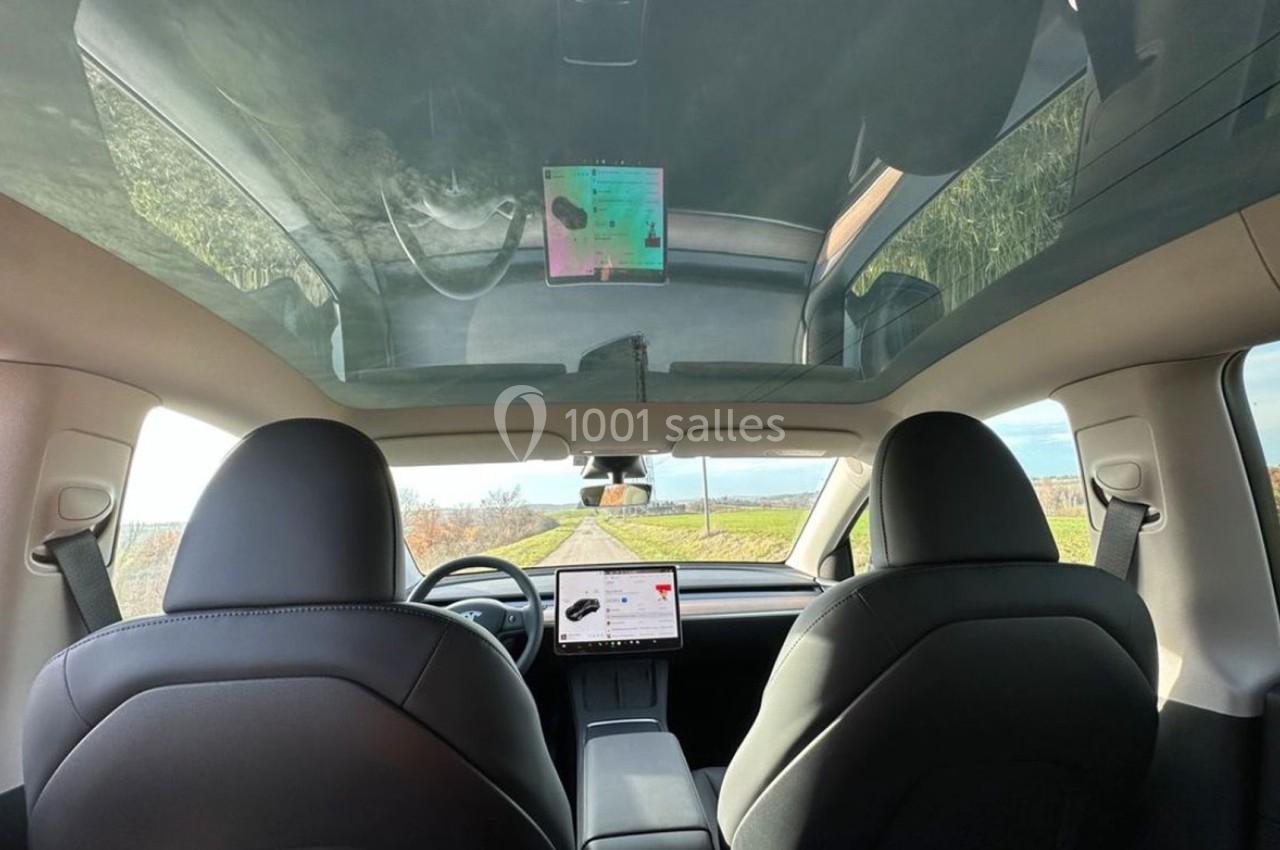 Vue intérieure d'une voiture avec un toit panoramique, montrant les sièges avant et un écran central affichant une carte.