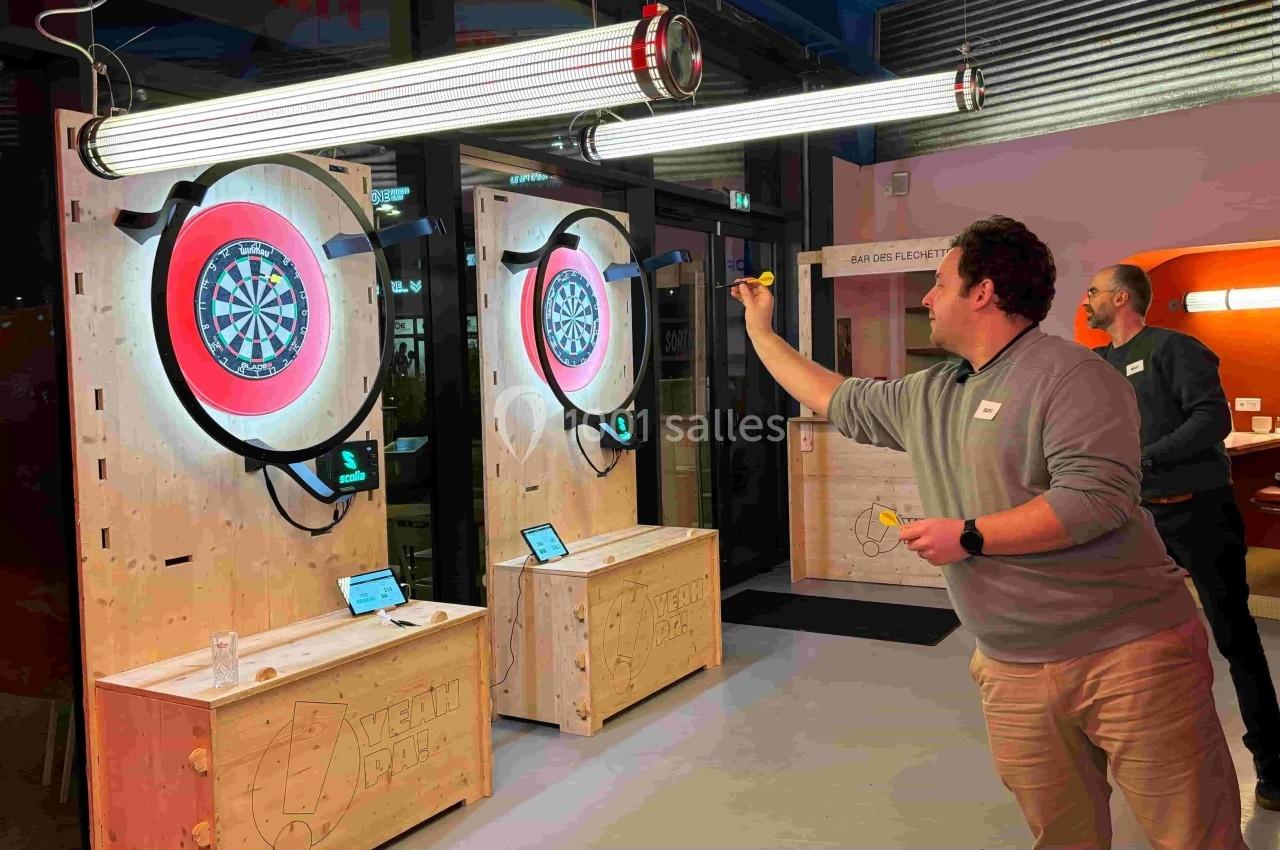 Un homme joue aux fléchettes électroniques dans un espace intérieur moderne, avec deux cibles lumineuses.