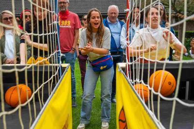 Des personnes jouent à un jeu de lancer de ballons de basket en plein air, entourées de spectateurs.