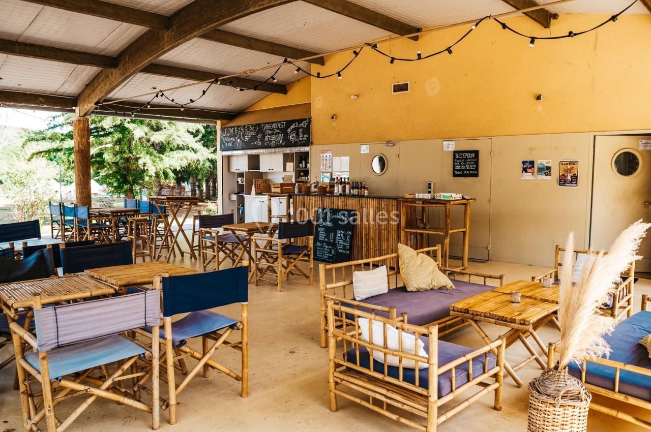 Espace extérieur couvert avec des tables et chaises en bambou, décoré de guirlandes lumineuses et d'affiches murales.