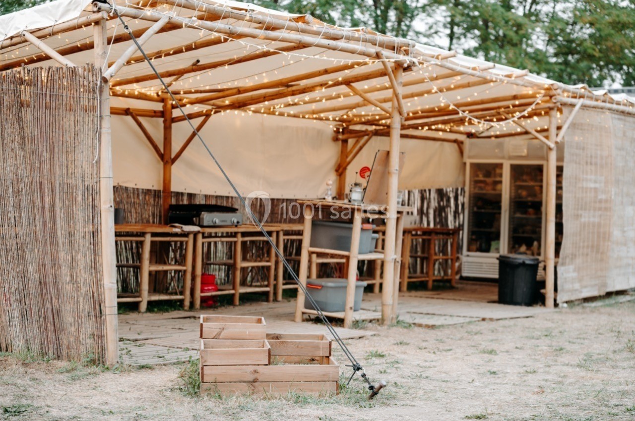 Abri en bois avec toit en toile, éclairé par des guirlandes lumineuses, abritant un comptoir et des équipements.