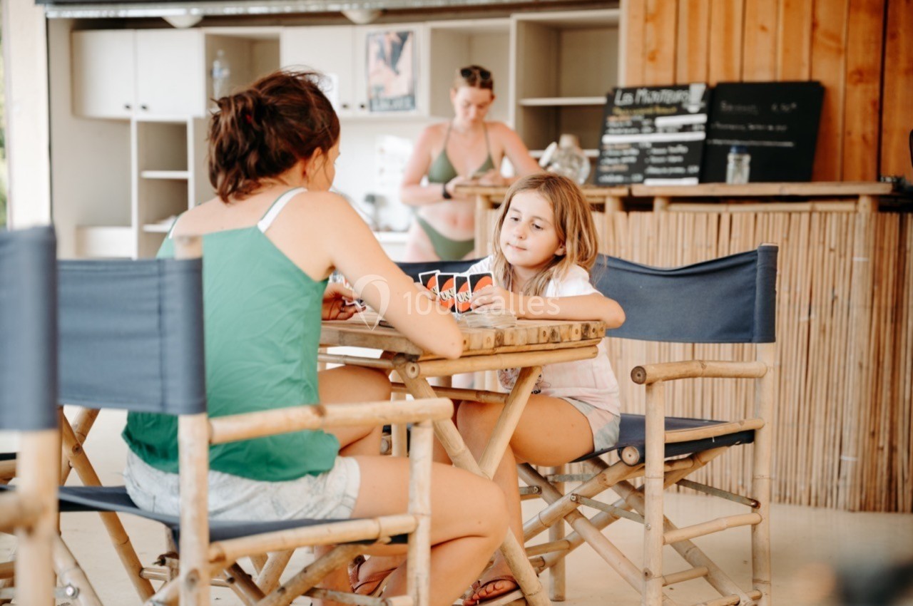 Une femme et une fillette jouent aux cartes à une table en bois dans un espace de restauration décontracté.