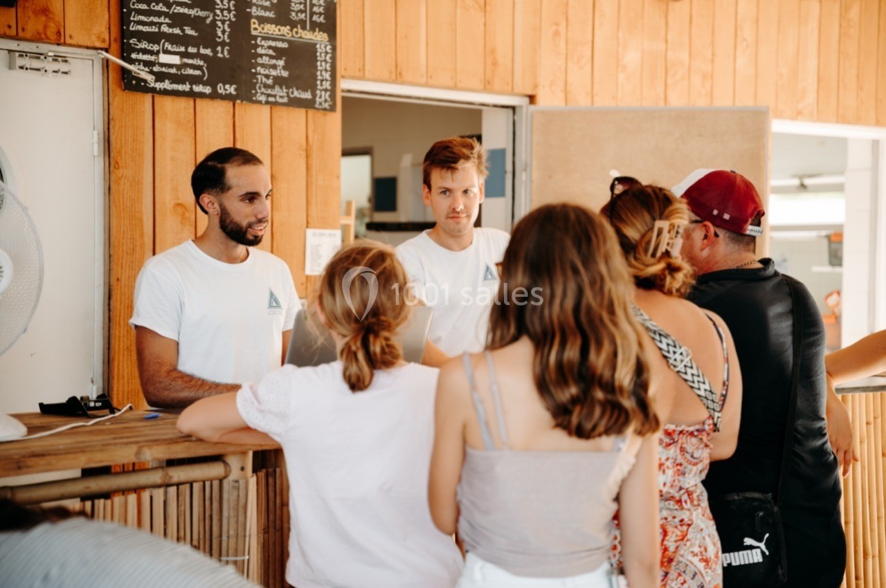 Des personnes commandent à un comptoir en bois où deux employés en t-shirts blancs les servent.