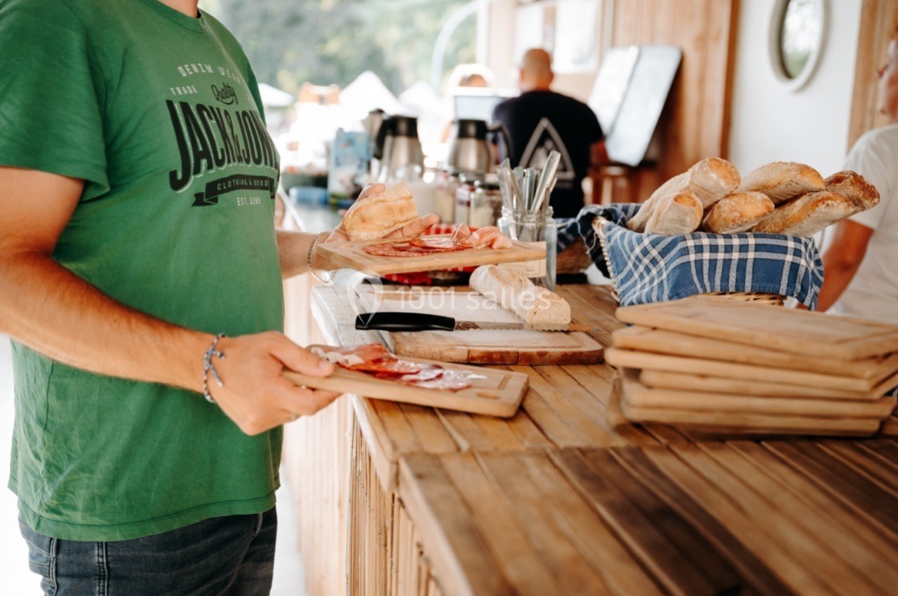 Un homme en t-shirt vert sert des planches de charcuterie et de pain dans un espace de restauration en bois.