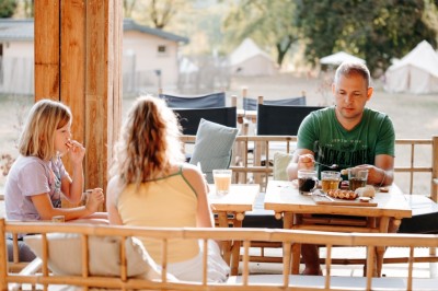 Deux personnes pratiquent le yoga en plein air sur des tapis, entourées de végétation.