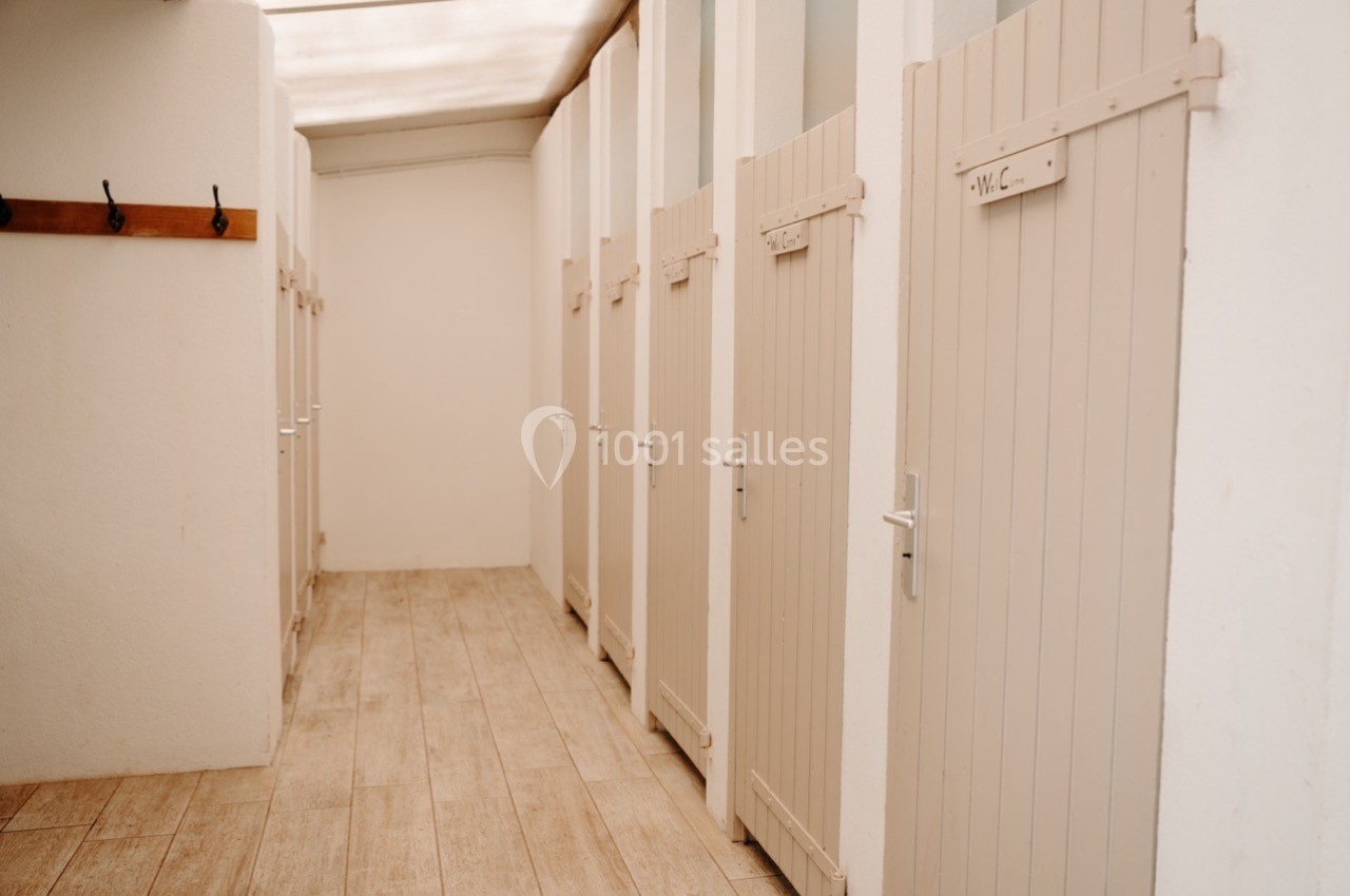 Rangée de cabines de toilettes avec portes en bois beige, sol en parquet clair et mur blanc.