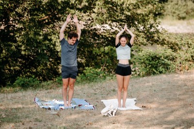 Deux personnes pratiquent le yoga en plein air sur des tapis, entourées de végétation.