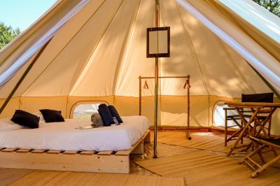 Intérieur d'une tente glamping avec un lit double, des meubles en bois et une ambiance lumineuse et chaleureuse.
