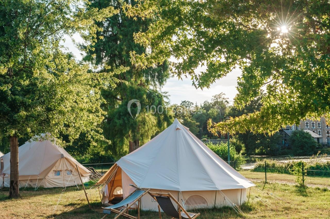 Tentes blanches installées dans un espace vert ensoleillé, entourées d'arbres et de végétation.