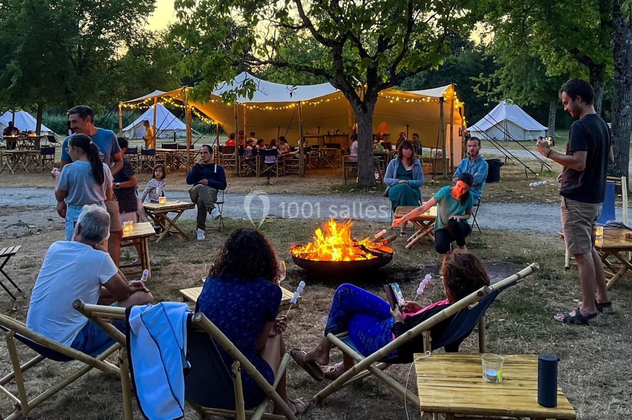 Des personnes assises autour d'un feu de camp dans un cadre extérieur avec des tentes éclairées en arrière-plan.