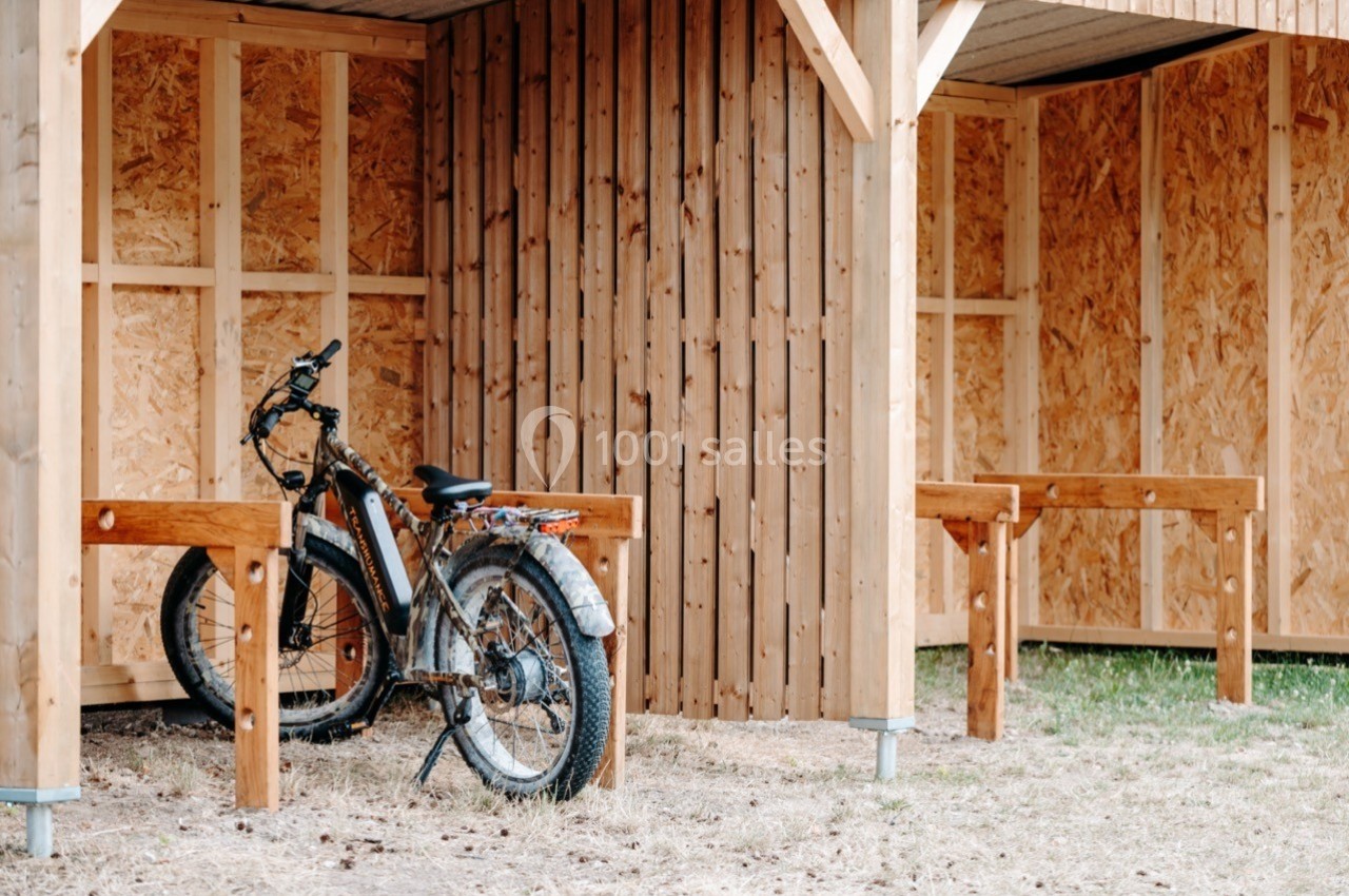 Abri en bois avec un vélo stationné, entouré de supports en bois sur un sol en herbe.