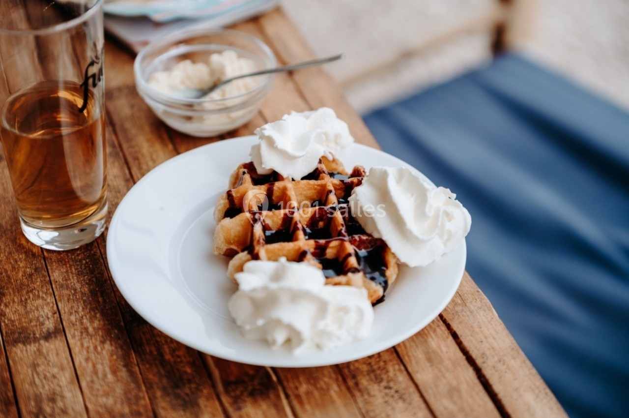 Assiette de gaufres garnies de crème chantilly et de sauce chocolat, posée sur une table en bois.