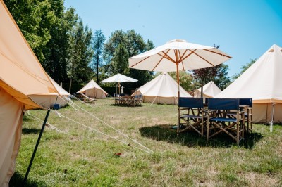 Miniature Location salle Cellettes (Loir-et-Cher) - Lodg’ing Nature Camp Châteaux de la Loire #12 Tentes blanches installées dans un espace naturel près d'une rivière, entourées d'arbres et d'un pont au coucher du soleil.