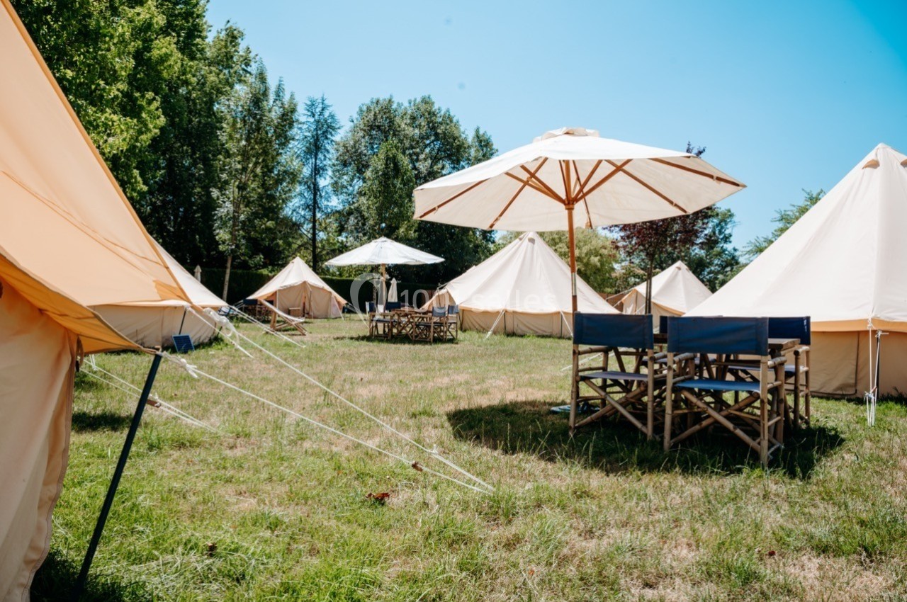 Tentes beige et chaises en bois sous des parasols sur une pelouse entourée d'arbres par temps ensoleillé.