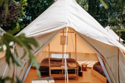 Miniature Location salle Cellettes (Loir-et-Cher) - Lodg’ing Nature Camp Châteaux de la Loire #9 Tentes blanches installées dans un espace naturel près d'une rivière, entourées d'arbres et d'un pont au coucher du soleil.