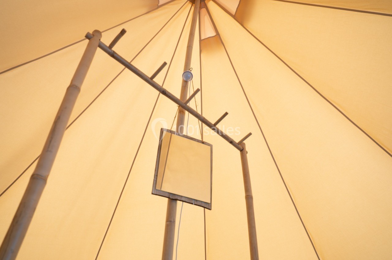 Structure en bambou sous une tente beige, avec un cadre suspendu au centre.