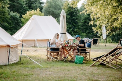 Miniature Location salle Cellettes (Loir-et-Cher) - Lodg’ing Nature Camp Châteaux de la Loire #19 Tentes blanches installées dans un espace naturel près d'une rivière, entourées d'arbres et d'un pont au coucher du soleil.