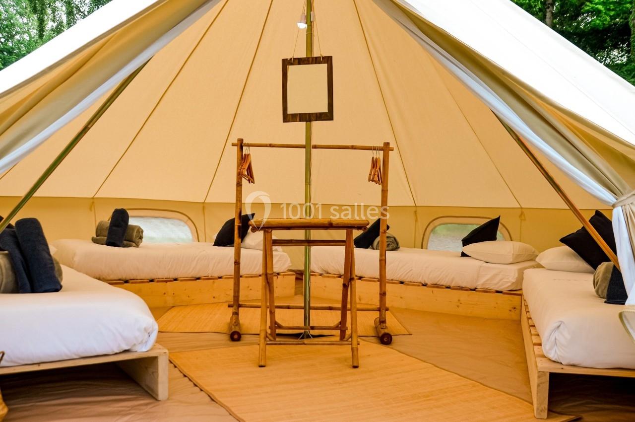 Intérieur d'une tente spacieuse avec lits simples, mobilier en bois et lumière naturelle entrant par l'ouverture.