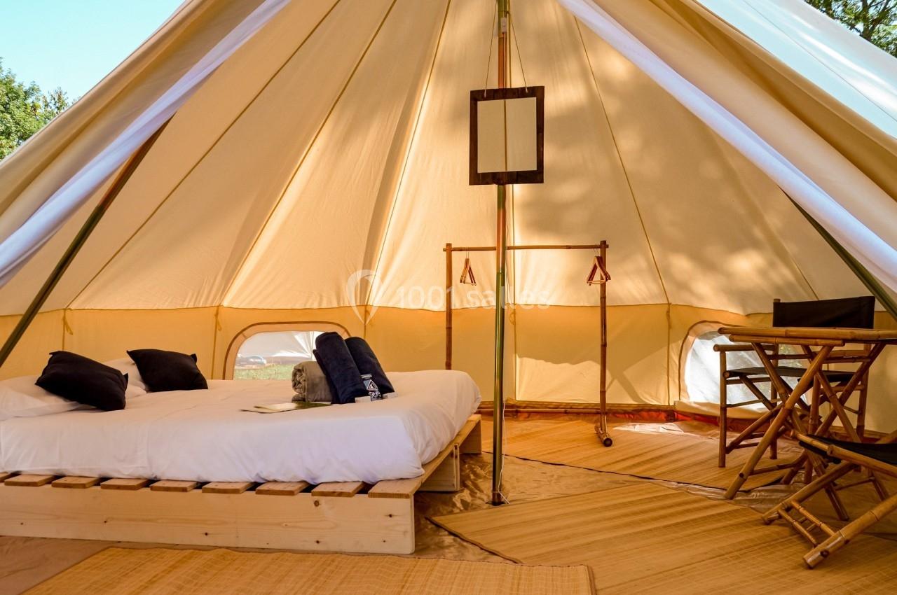 Intérieur d'une tente spacieuse avec lit double, mobilier en bois, tapis et lumière naturelle.
