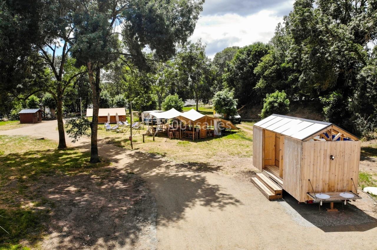 Vue d'un espace extérieur avec cabanes en bois, tentes et arbres, dans un cadre naturel ensoleillé.