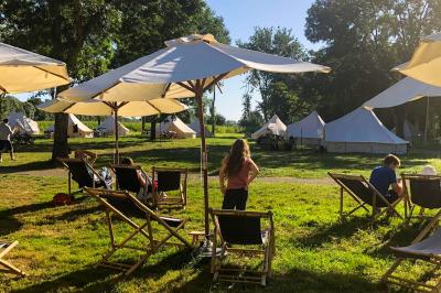 Cuisine extérieure en bambou avec plan de travail, tabouret, réfrigérateur, ustensiles et vaisselle dans un cadre naturel.