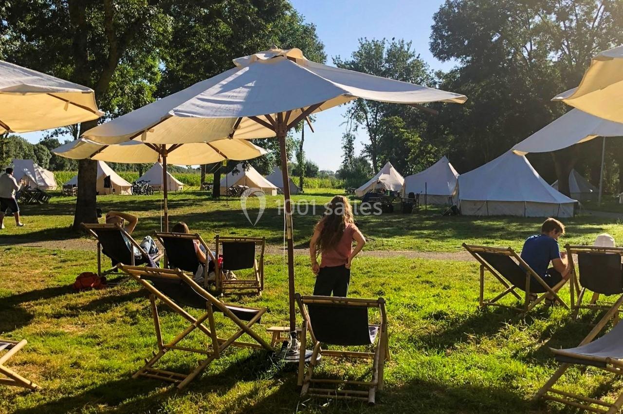 Chaises longues et parasols sur une pelouse ensoleillée, avec des tentes blanches en arrière-plan dans un cadre naturel.