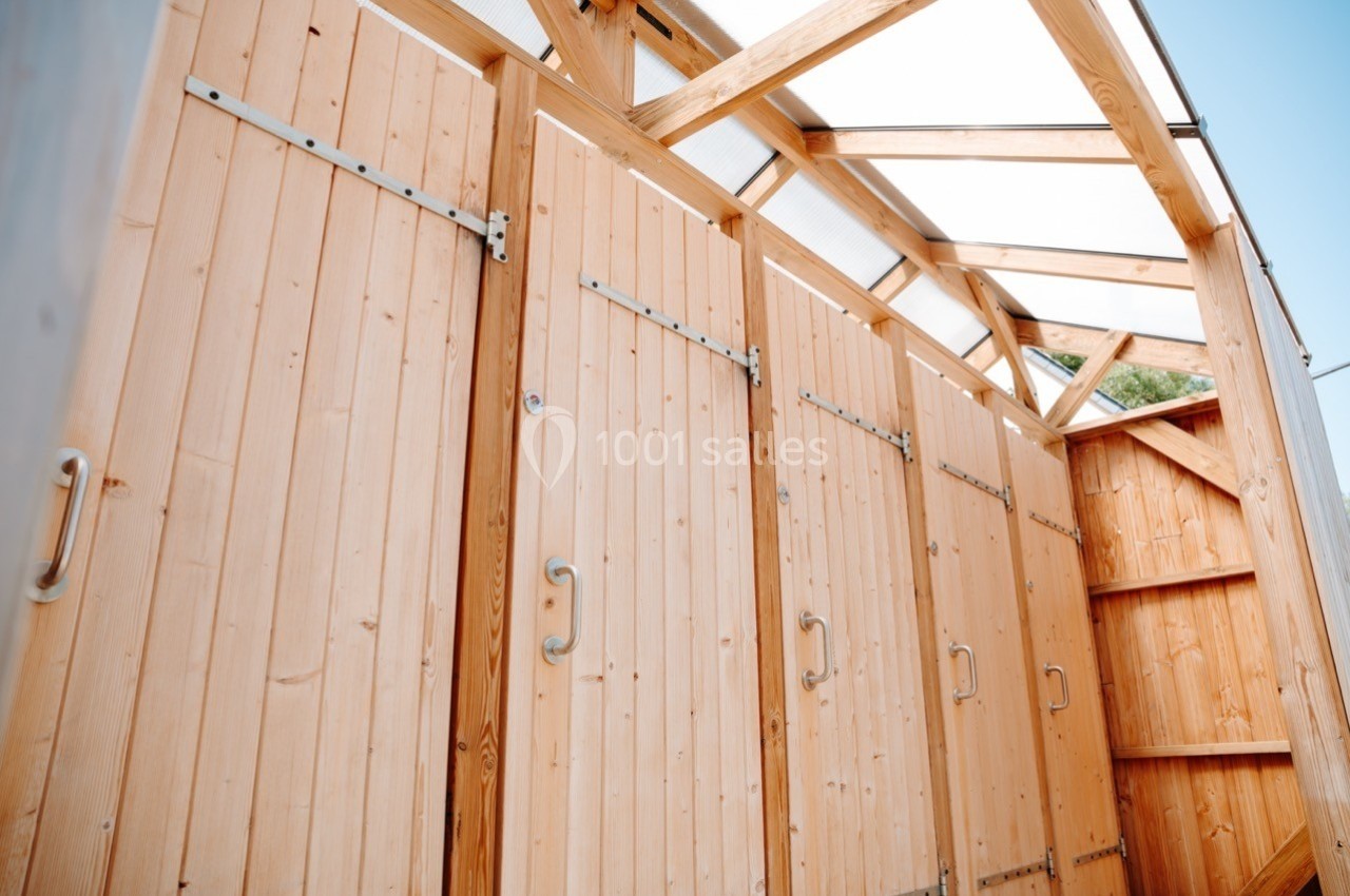 Cabines en bois avec portes alignées, sous une structure en bois et toit translucide.