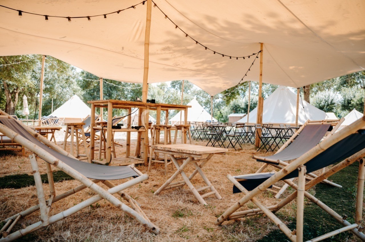 Chaises longues et tables en bois sous une tente blanche dans un espace extérieur ombragé.