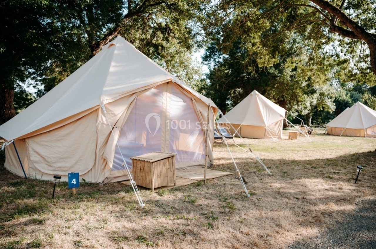 Tentes en toile beige installées sur une pelouse, entourées d'arbres, avec des coffres en bois à l'entrée.