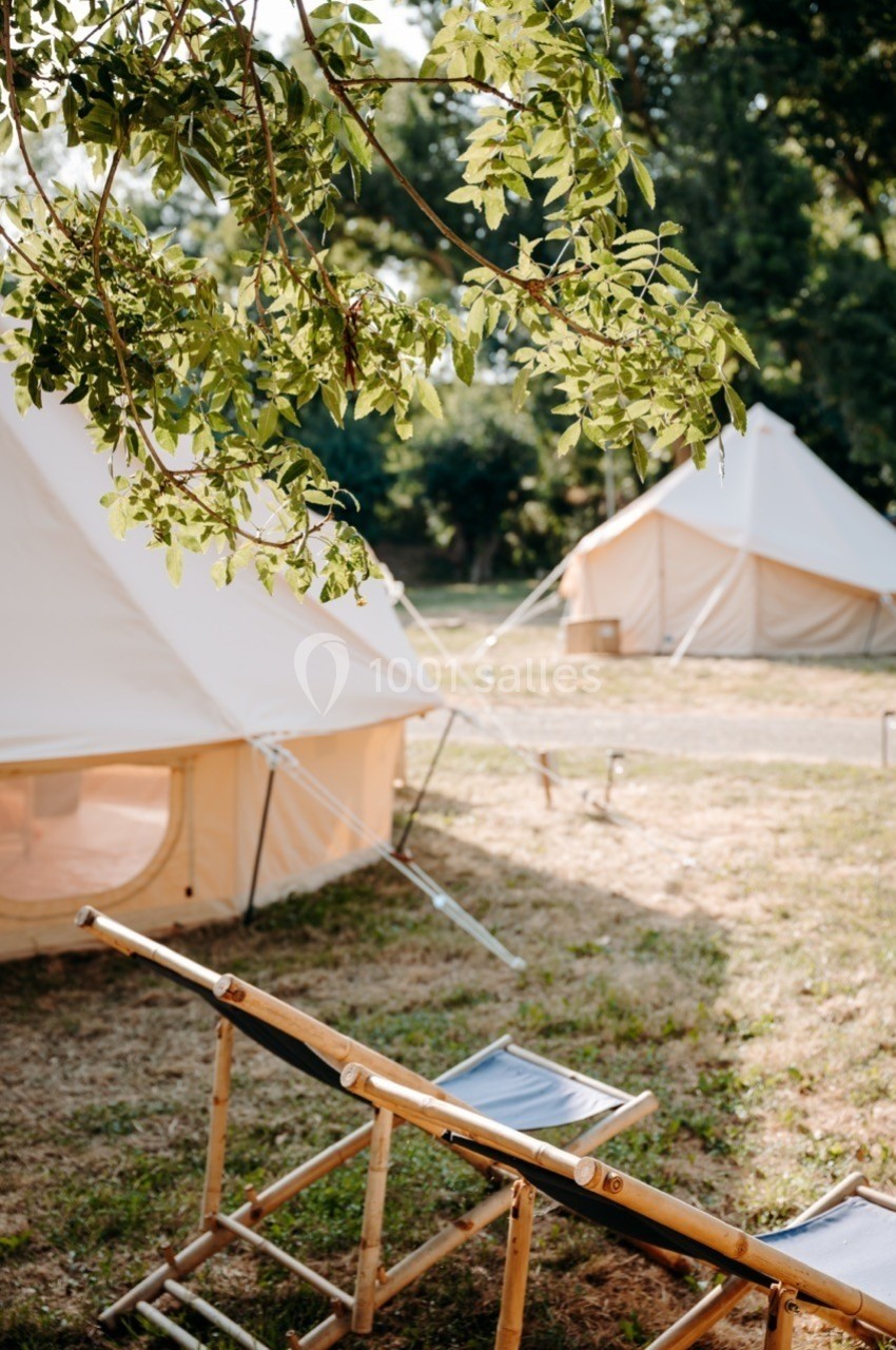 Deux tentes en toile beige installées dans un espace naturel, avec une chaise pliante en bois au premier plan.