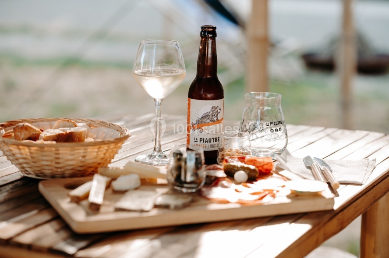 Planche de fromages et charcuteries accompagnée de pain, bière artisanale et verre de vin sur une table en bois.