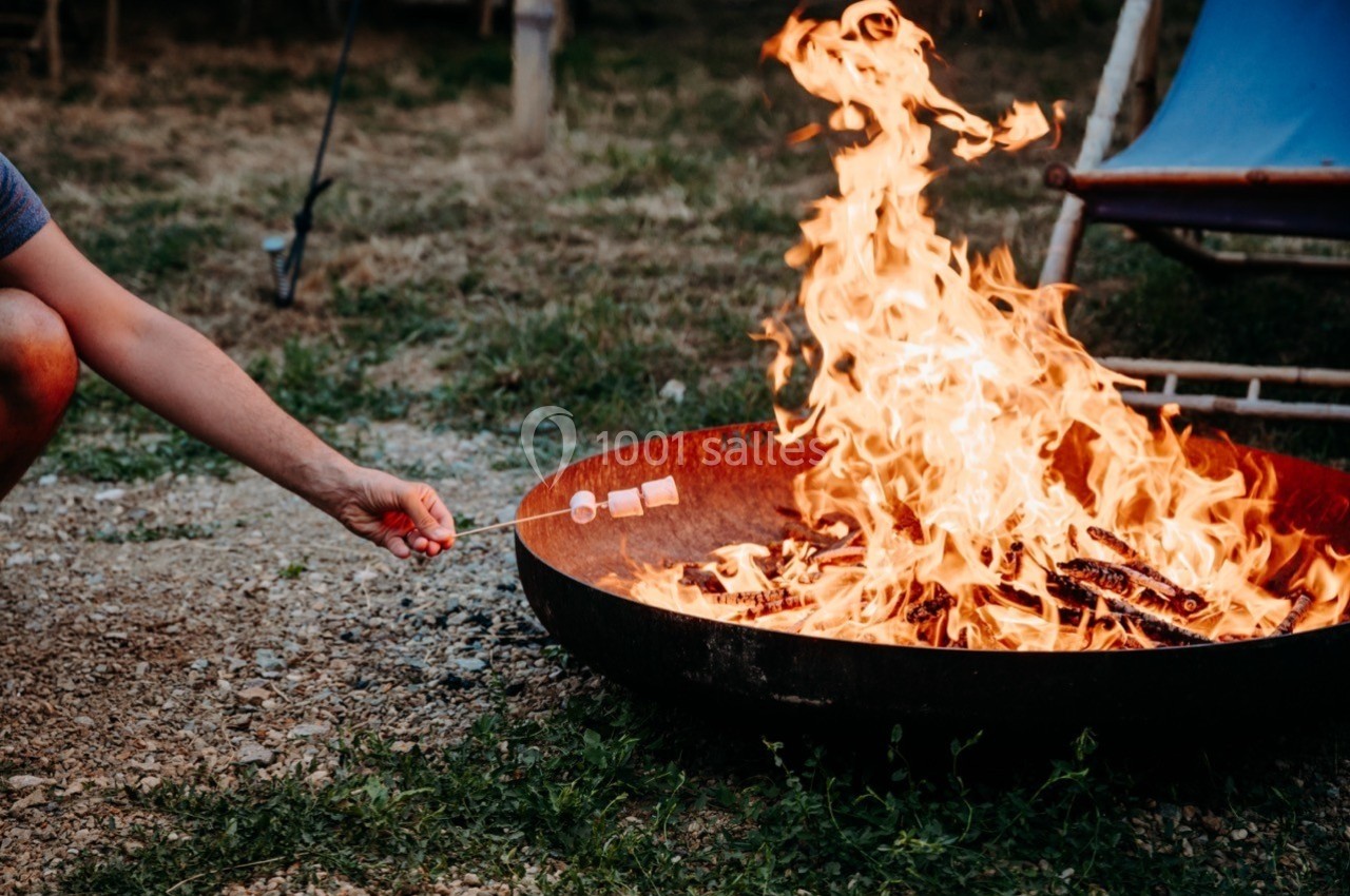 Une personne fait griller des guimauves au-dessus d'un feu de camp dans un grand brasero en plein air.