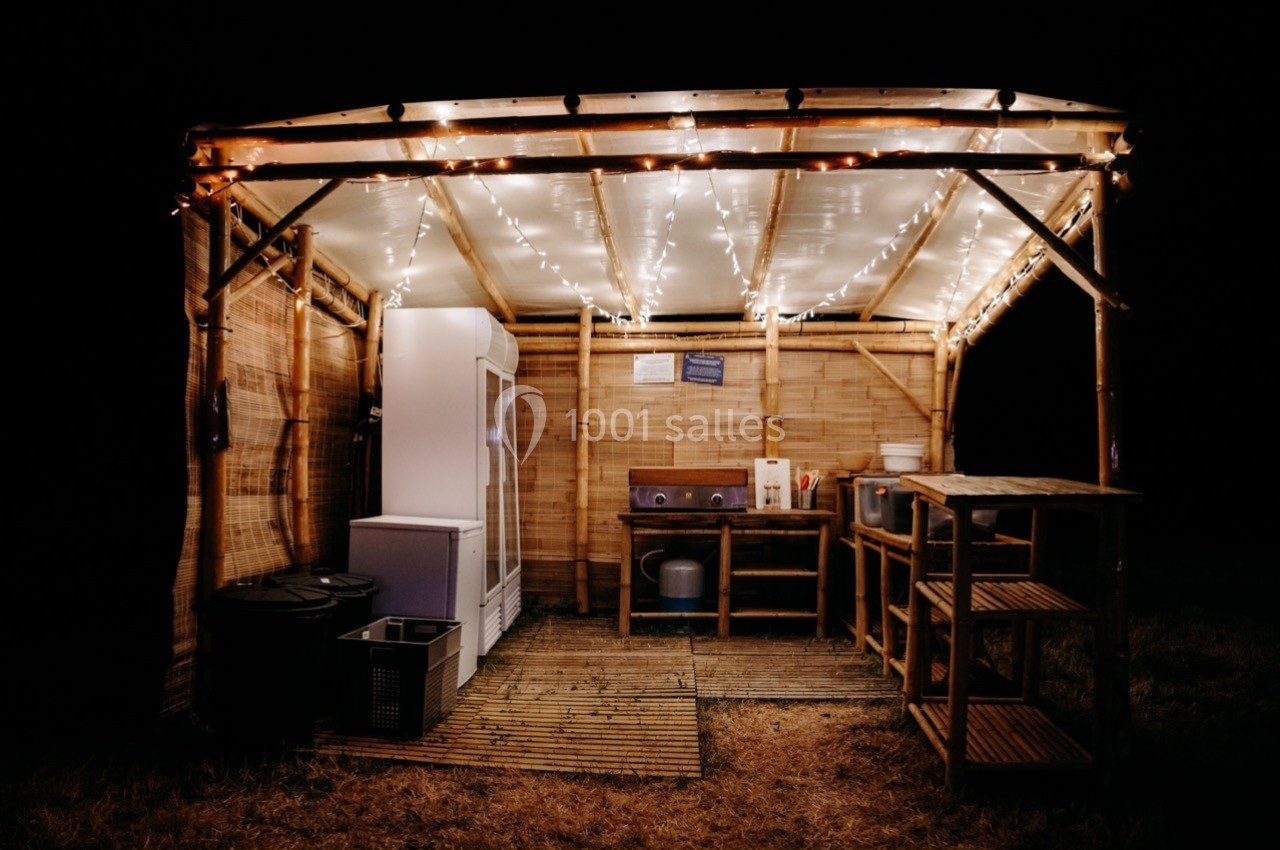 Cuisine extérieure en bois éclairée par des guirlandes lumineuses, équipée de rangements, d'un évier et d'un réfrigérateur.