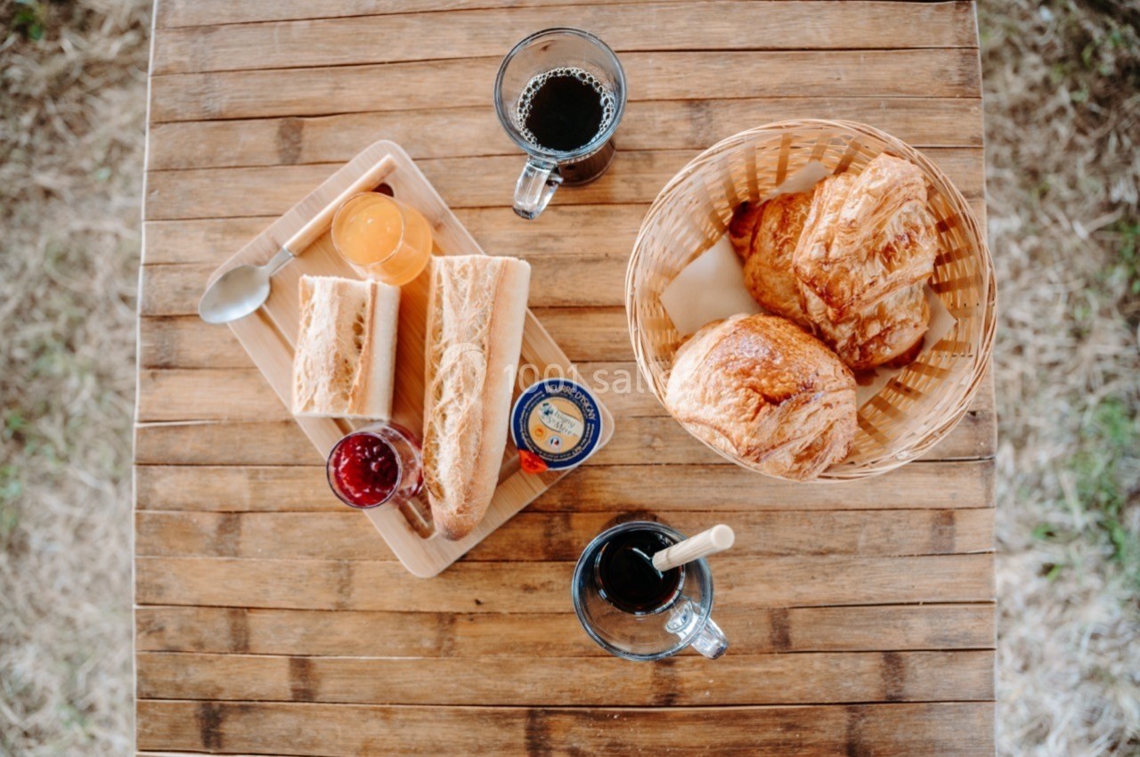 Petit-déjeuner avec croissants, baguettes, confitures, jus d'orange et café sur une table en bois.