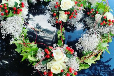 Jeune femme portant une couronne de fleurs blanches, vêtue de dentelle blanche, dans un jardin verdoyant.