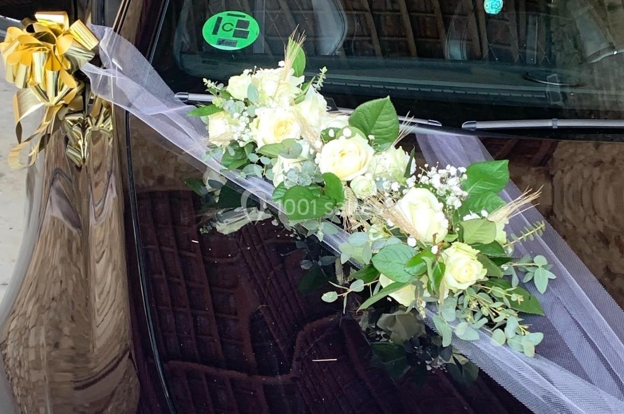 Décoration florale blanche et verte avec rubans dorés sur le capot d'une voiture dans un garage.