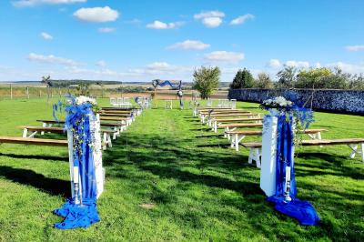 Jeune femme portant une couronne de fleurs blanches, vêtue de dentelle blanche, dans un jardin verdoyant.