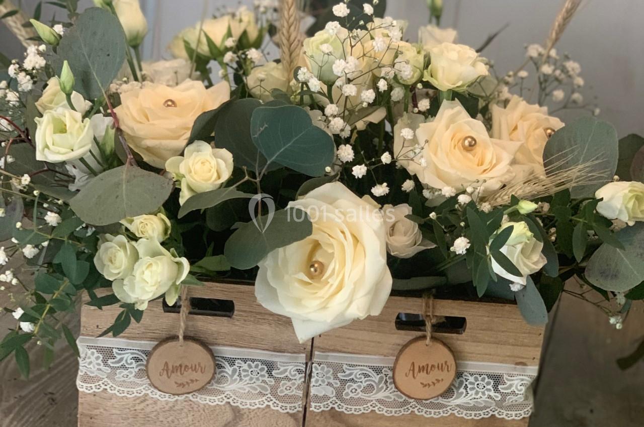 Arrangement floral avec des roses blanches et feuillage dans des caisses en bois décorées de dentelle.