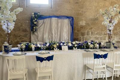 Jeune femme portant une couronne de fleurs blanches, vêtue de dentelle blanche, dans un jardin verdoyant.