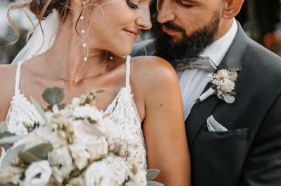 Jeune femme portant une couronne de fleurs blanches, vêtue de dentelle blanche, dans un jardin verdoyant.