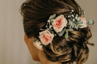 Jeune femme portant une couronne de fleurs blanches, vêtue de dentelle blanche, dans un jardin verdoyant.