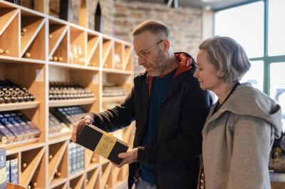 Un homme et une femme regardent une boîte dans un magasin de vins avec des étagères remplies de bouteilles en arrière-plan.