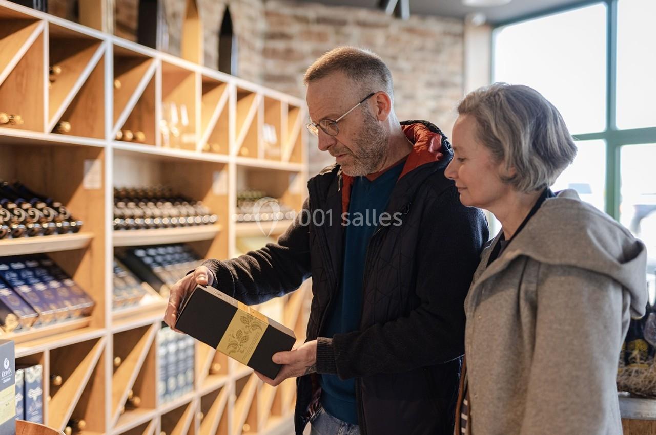 Un homme et une femme regardent une boîte dans un magasin de vins avec des étagères remplies de bouteilles en arrière-plan.