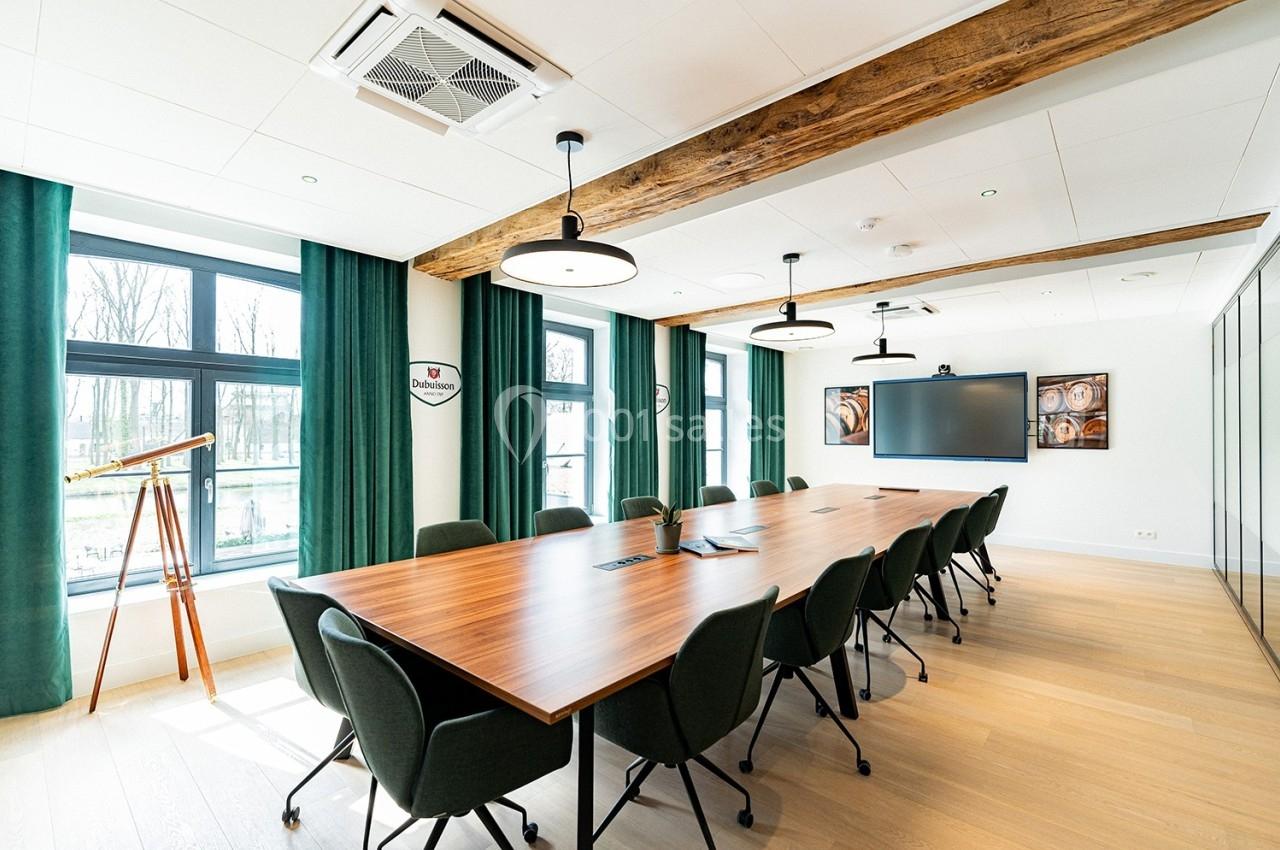Salle de réunion lumineuse avec grande table en bois, chaises noires, écran mural et fenêtres donnant sur l'extérieur.