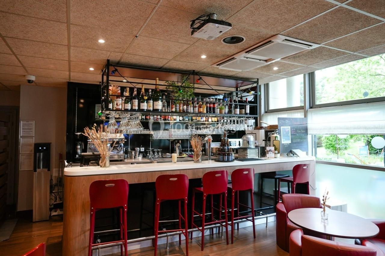 Bar moderne avec comptoir en marbre, tabourets rouges, étagères garnies de bouteilles et lumière naturelle.