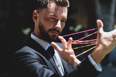 Homme en costume debout près d'une bibliothèque en bois, avec son ombre projetée sur un mur éclairé.