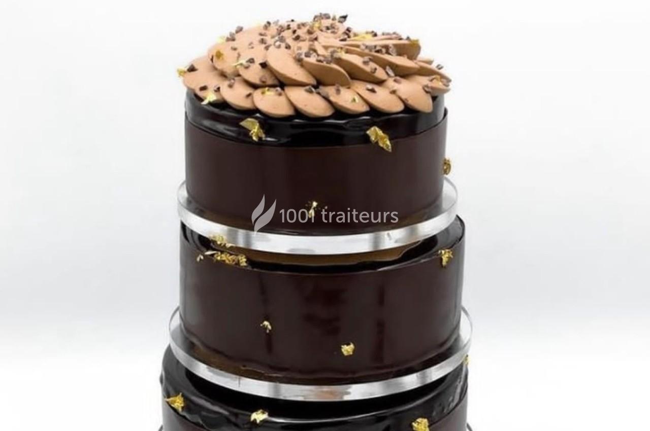 Gâteau à trois étages recouvert de glaçage au chocolat brillant, décoré de touches dorées et d'une garniture chocolatée.
