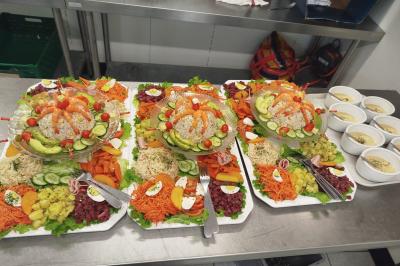 Buffet avec assortiments de sandwichs, samoussas, mini-burgers, canapés et coupes de fruits sur une table blanche.