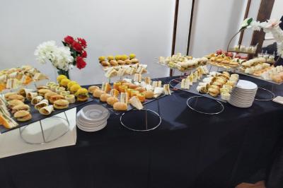 Buffet avec assortiments de sandwichs, samoussas, mini-burgers, canapés et coupes de fruits sur une table blanche.